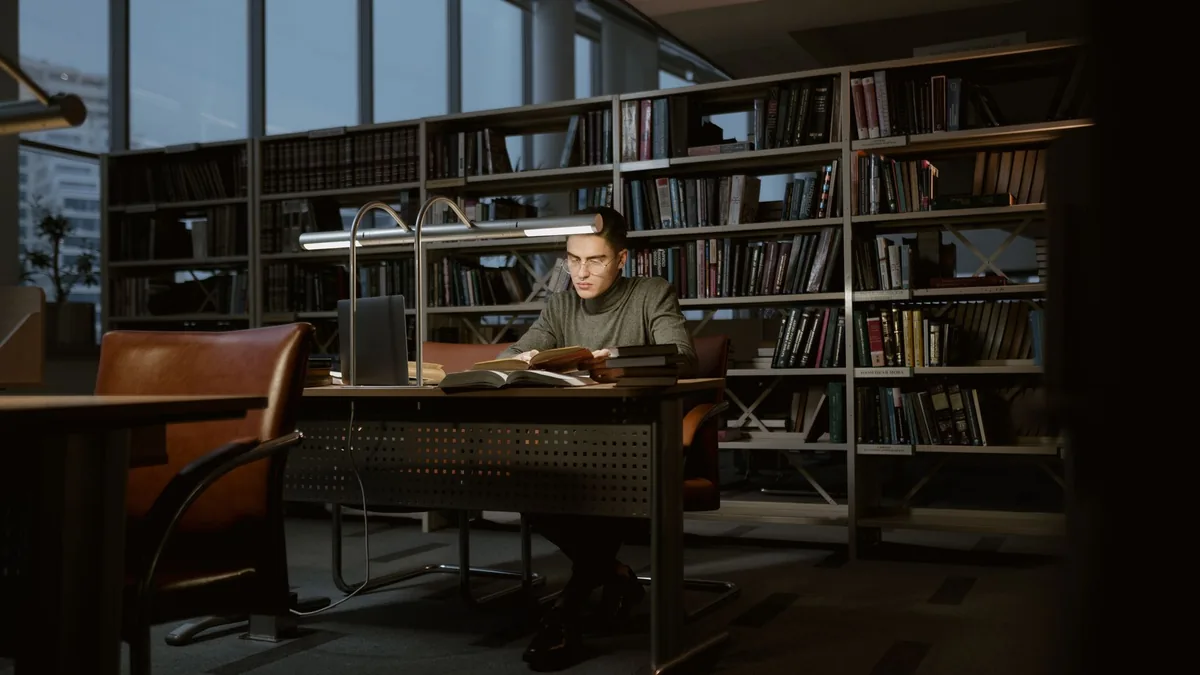 Man studying alone at a desk in a quiet, book-lined library