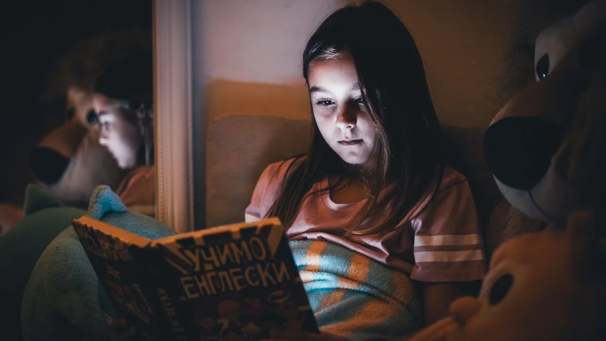 Girl reading a book in bed by the glow of a night light