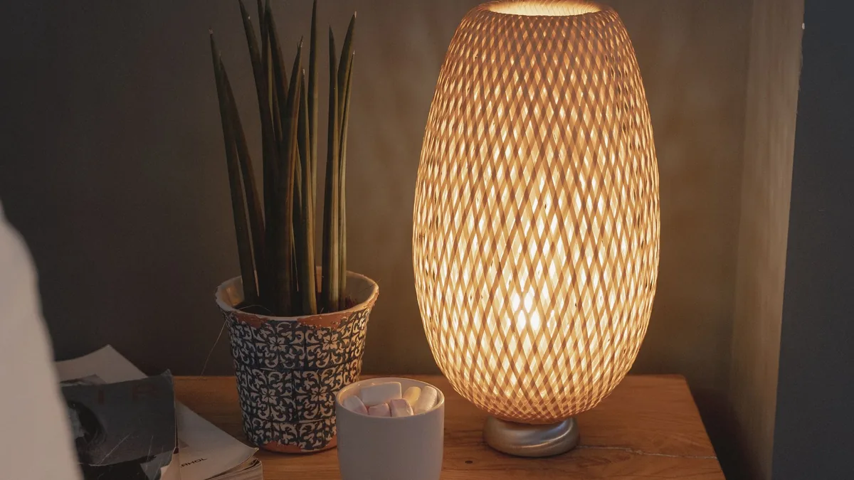 Woven lamp glowing on a bedside table next to a potted plant