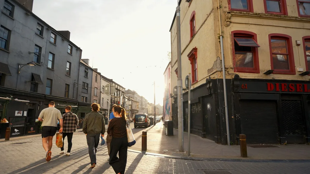 People walking along a sunlit city street of old buildings
