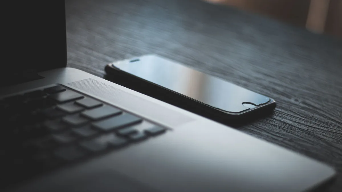 Laptop and smartphone side by side on a dark wooden desk