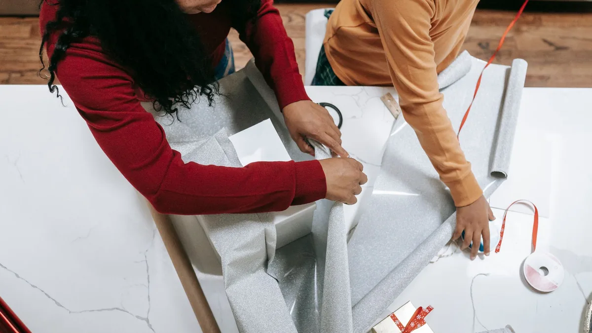 Woman and child wrapping a Christmas present in white paper at a table