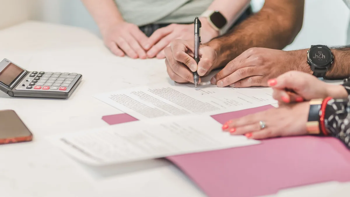 Two people signing a loan agreement beside a calculator