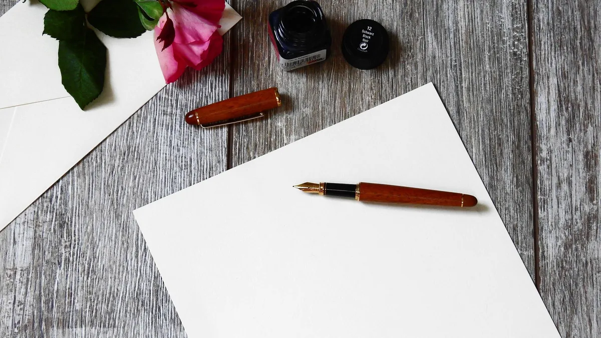 Fountain pen and a rose on a sheet of paper on a rustic wooden table