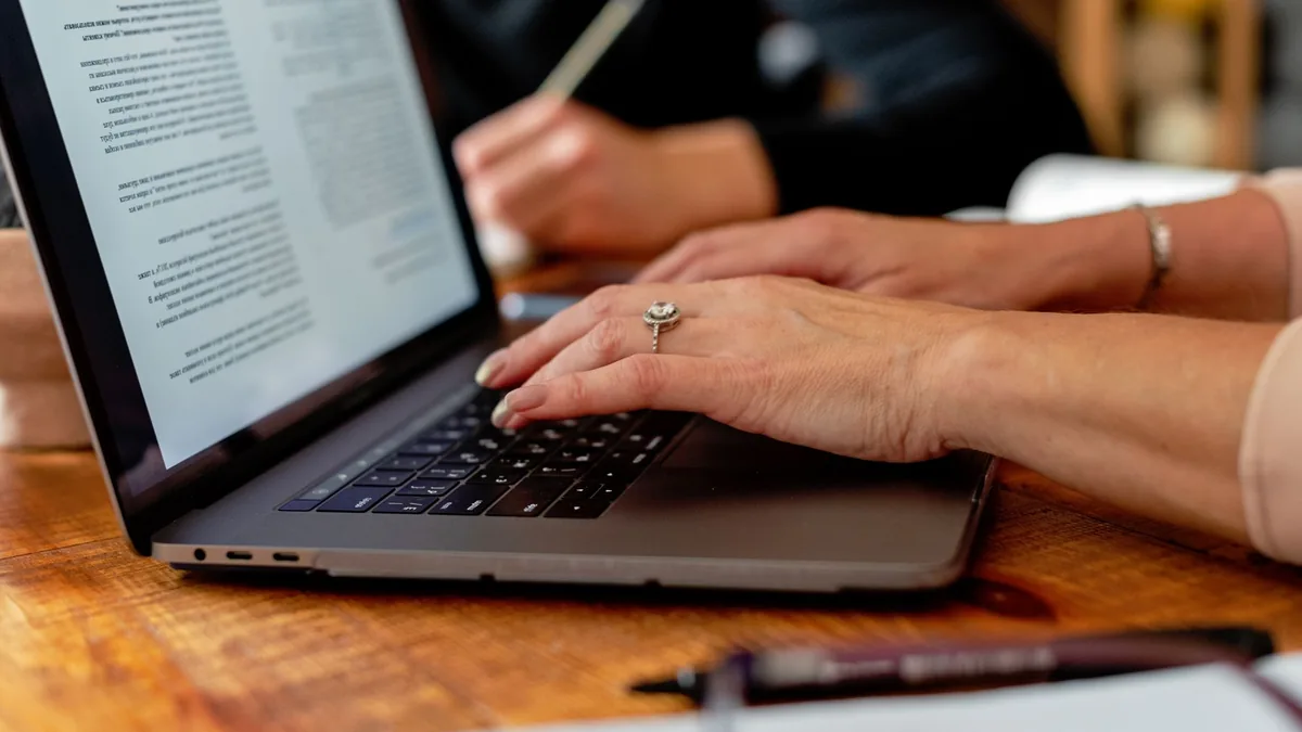 Hands typing on a laptop showing a document on a wooden desk