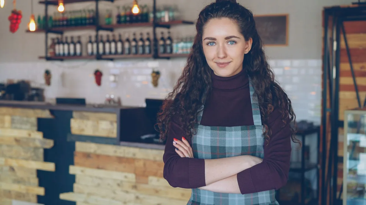 Café owner standing with arms folded inside her cosy coffee shop