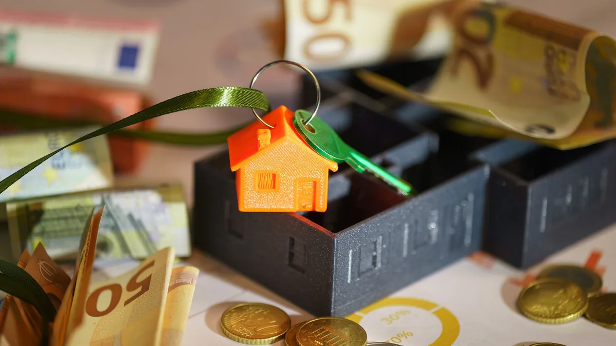 House-shaped keyring with keys, banknotes and coins on a table