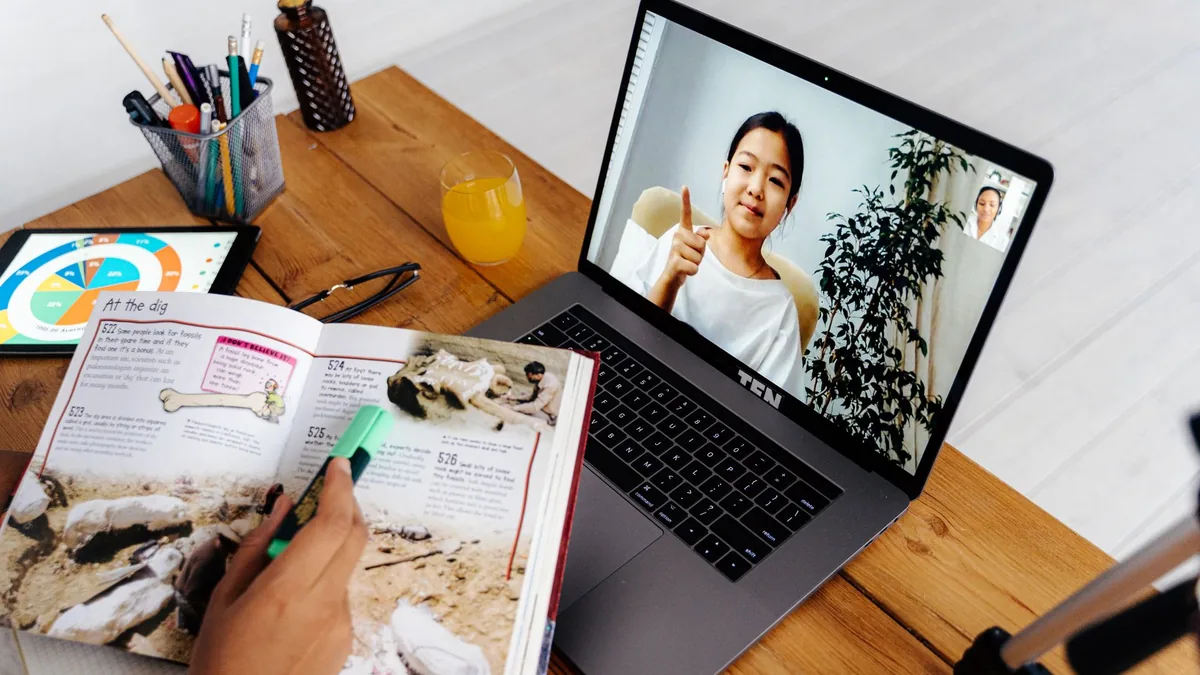 Laptop showing an online lesson next to an open textbook