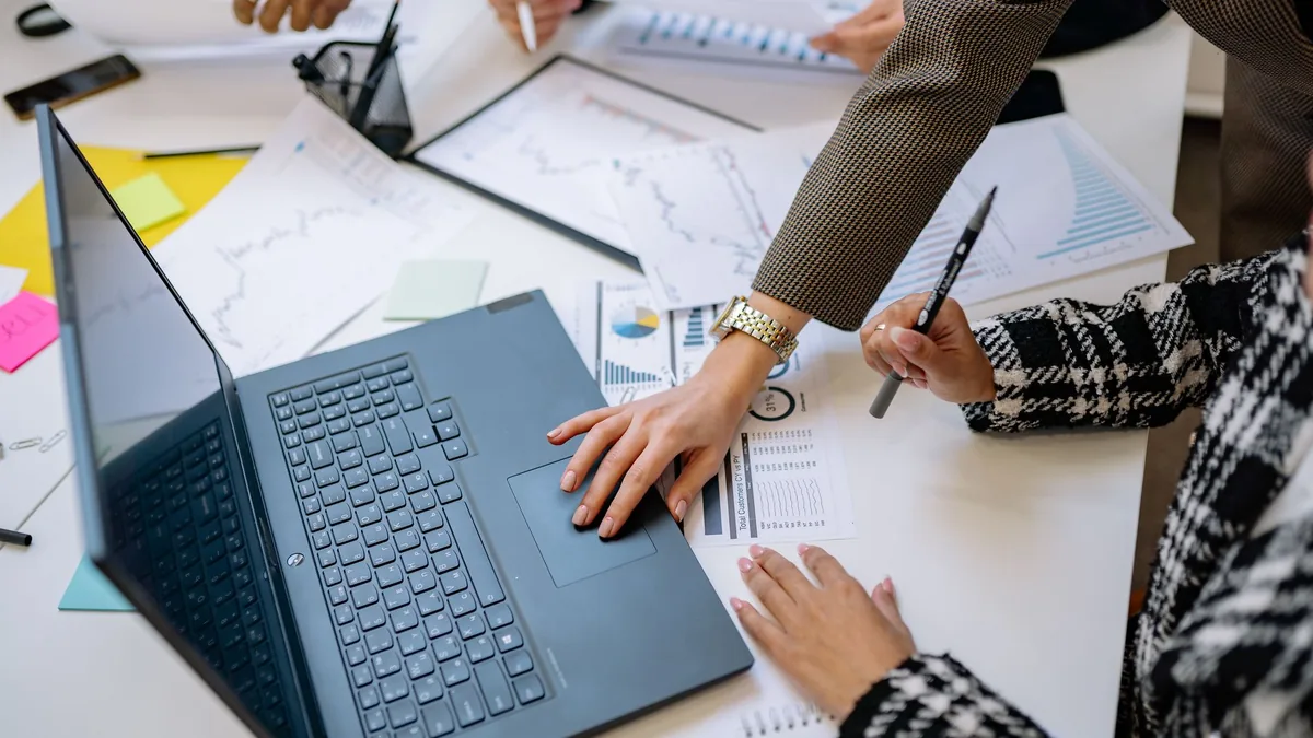 People reviewing financial charts and documents around a laptop at a meeting table
