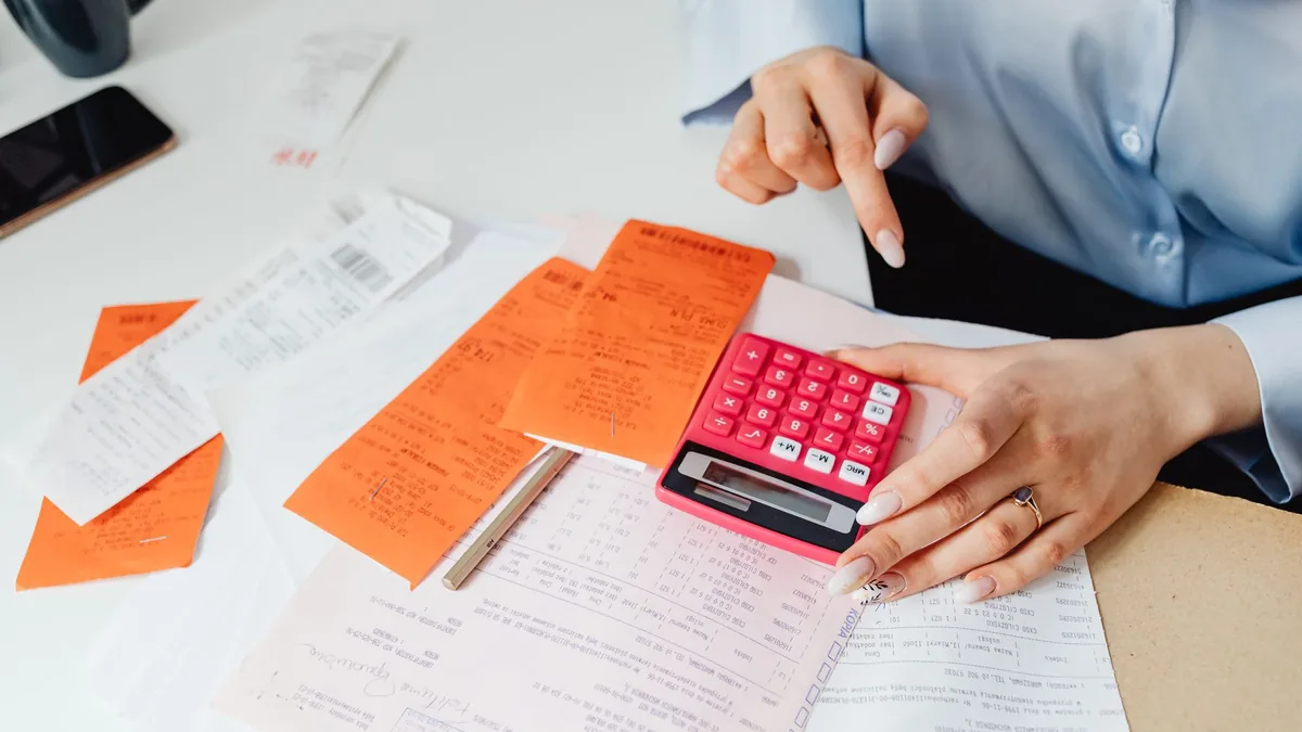 Woman working through receipts with a pink calculator at her desk