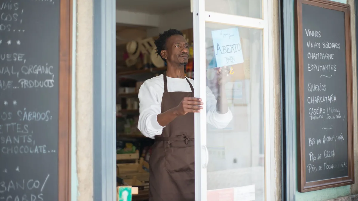 Shopkeeper in an apron opening the door of a small grocery shop