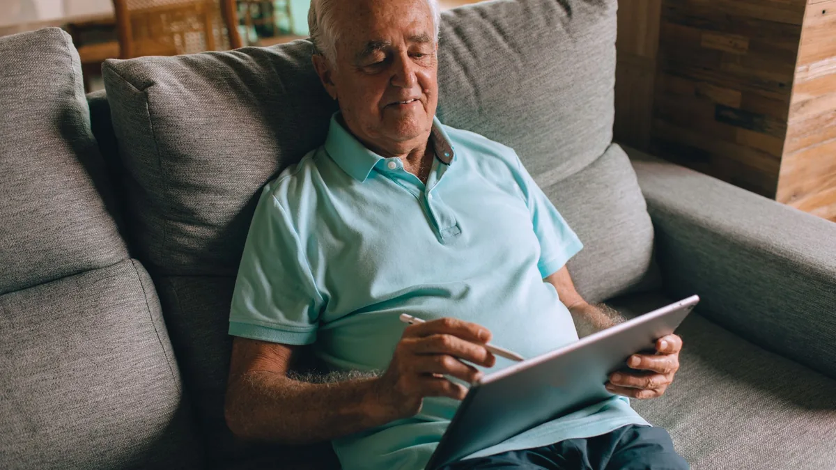 Older man sitting on a sofa using a tablet and stylus