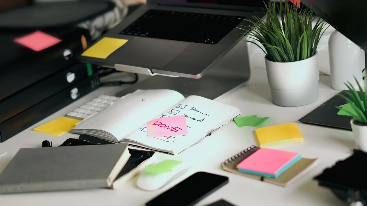 Office desk with a laptop, notebooks, checklists and colourful sticky notes