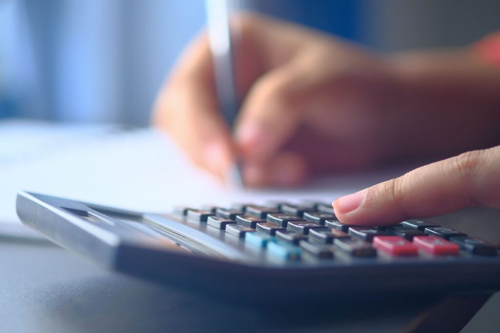 Close-up of a hand using a calculator while writing down figures, double-checking a budget