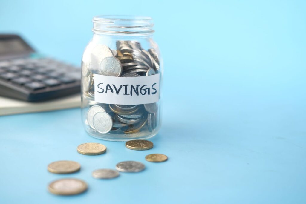 Glass jar labelled Savings filled with coins next to a calculator, representing an emergency fund