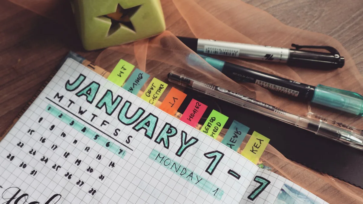 Planner open at January with colourful tabs and pens on a wooden desk