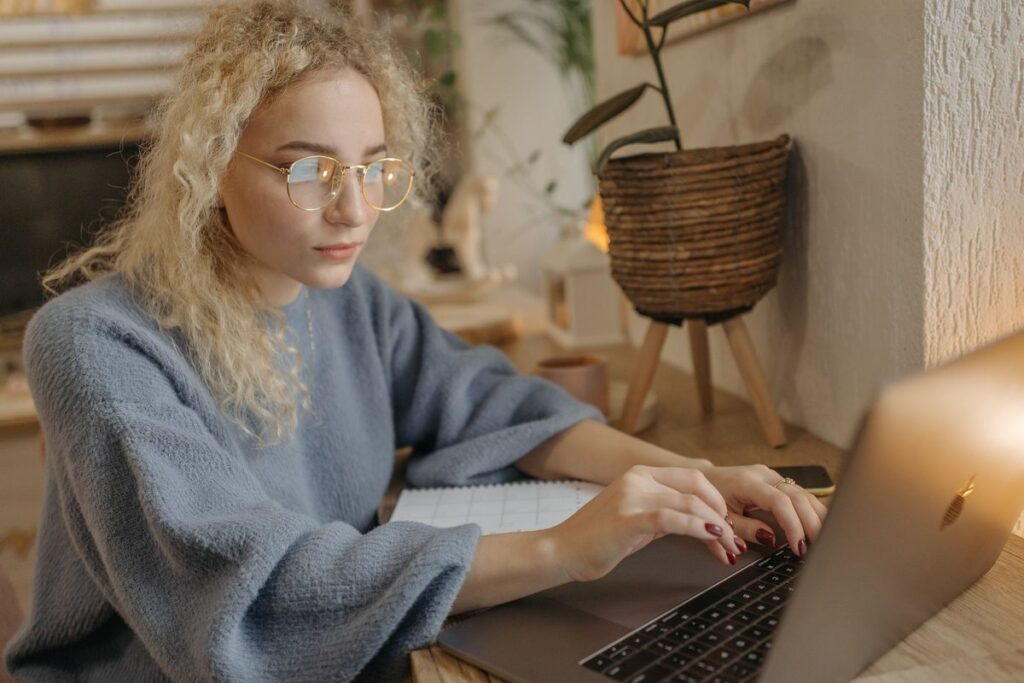 Woman with curly hair typing on a laptop at home, tailoring her CV to a job advert with help from AI