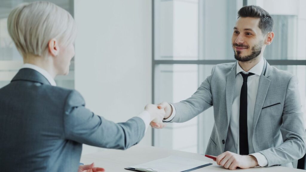 Two people shaking hands across a desk in a bright office after agreeing a job offer