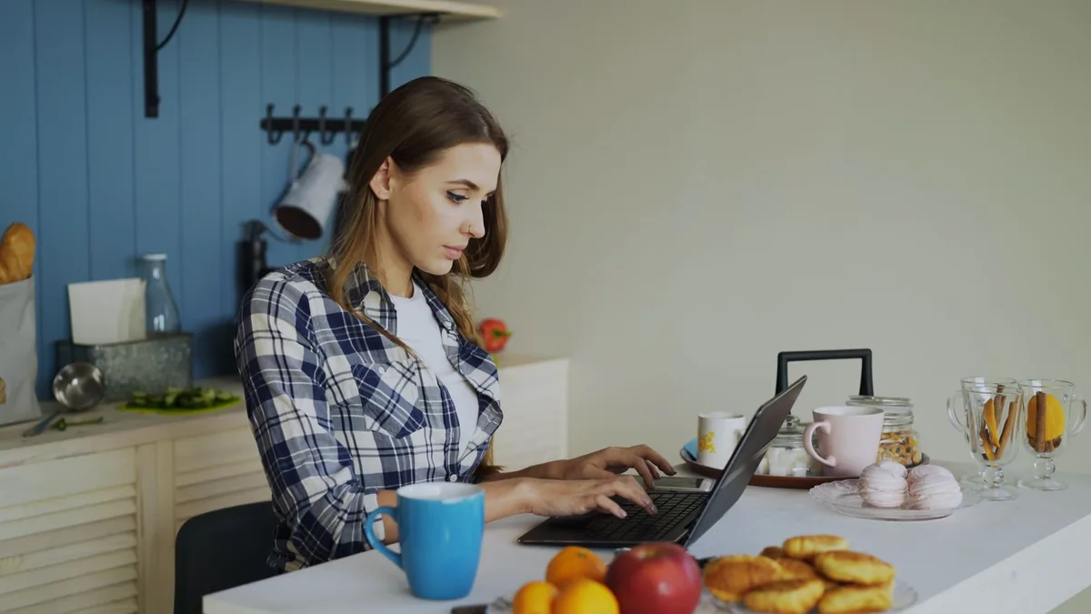 Woman using a laptop at her kitchen table at home, searching and applying for jobs in the UK