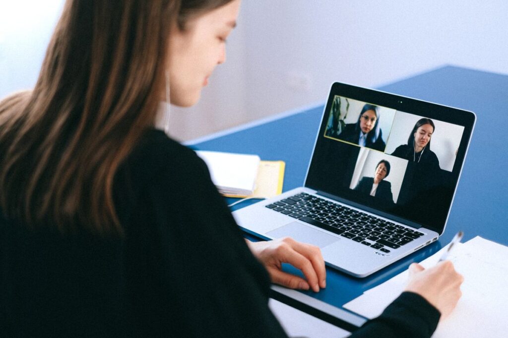 Woman taking notes during a video interview on her laptop, with several interviewers on screen