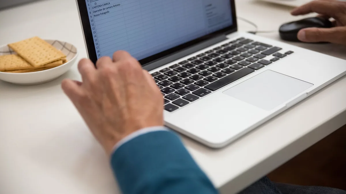 Person working on a laptop at a desk with a snack beside them