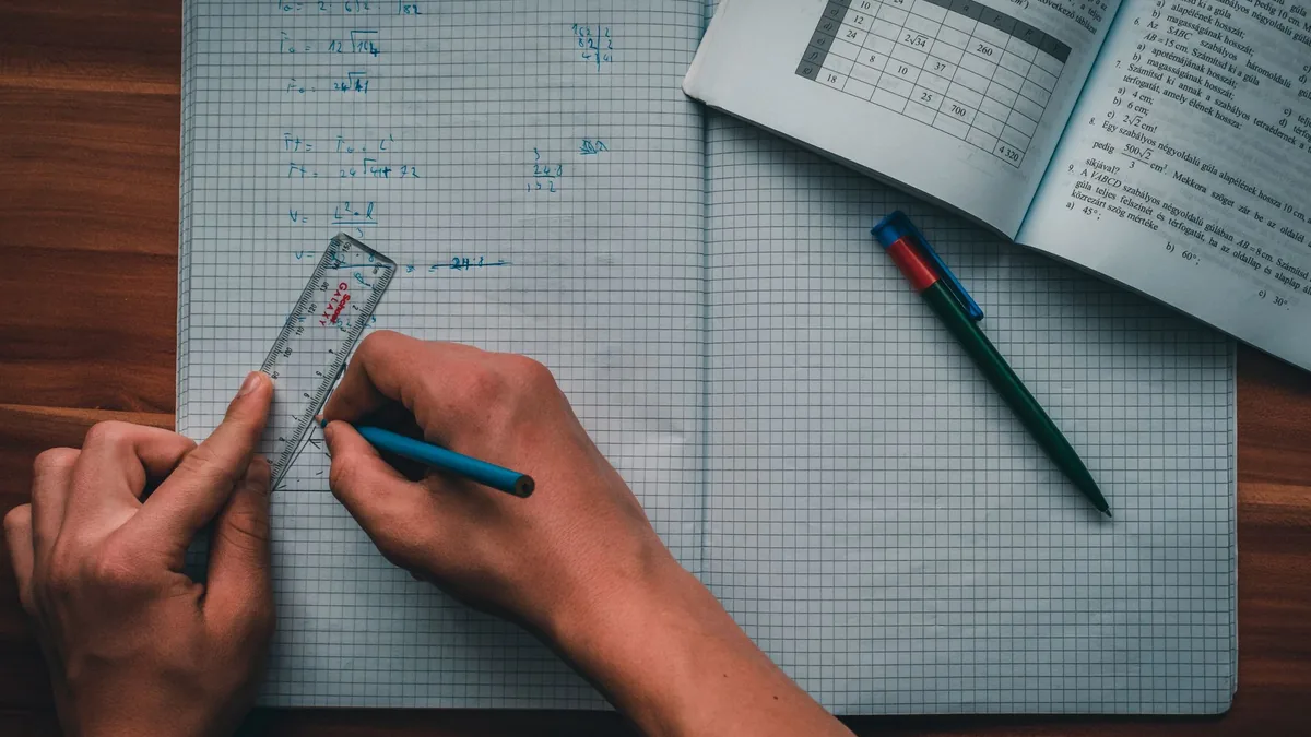 Person working through maths problems in a squared notebook with a ruler