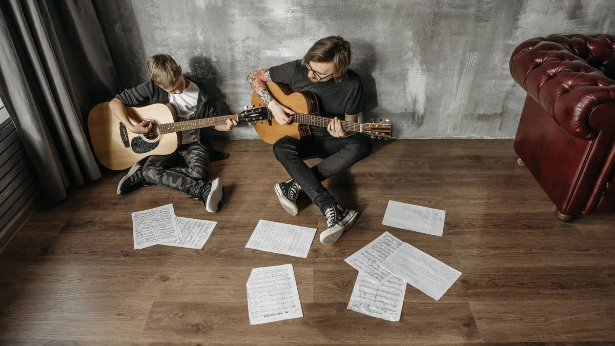Adult and teenager practising guitar on the floor surrounded by sheet music