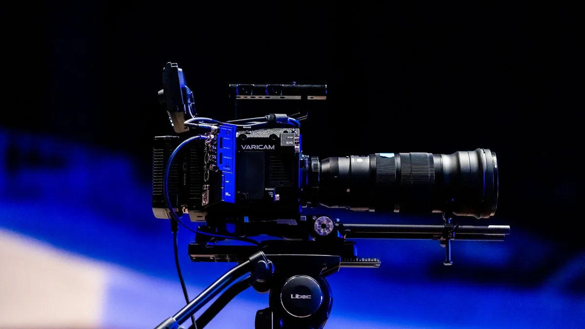 Professional video camera on a tripod against a blue-lit background