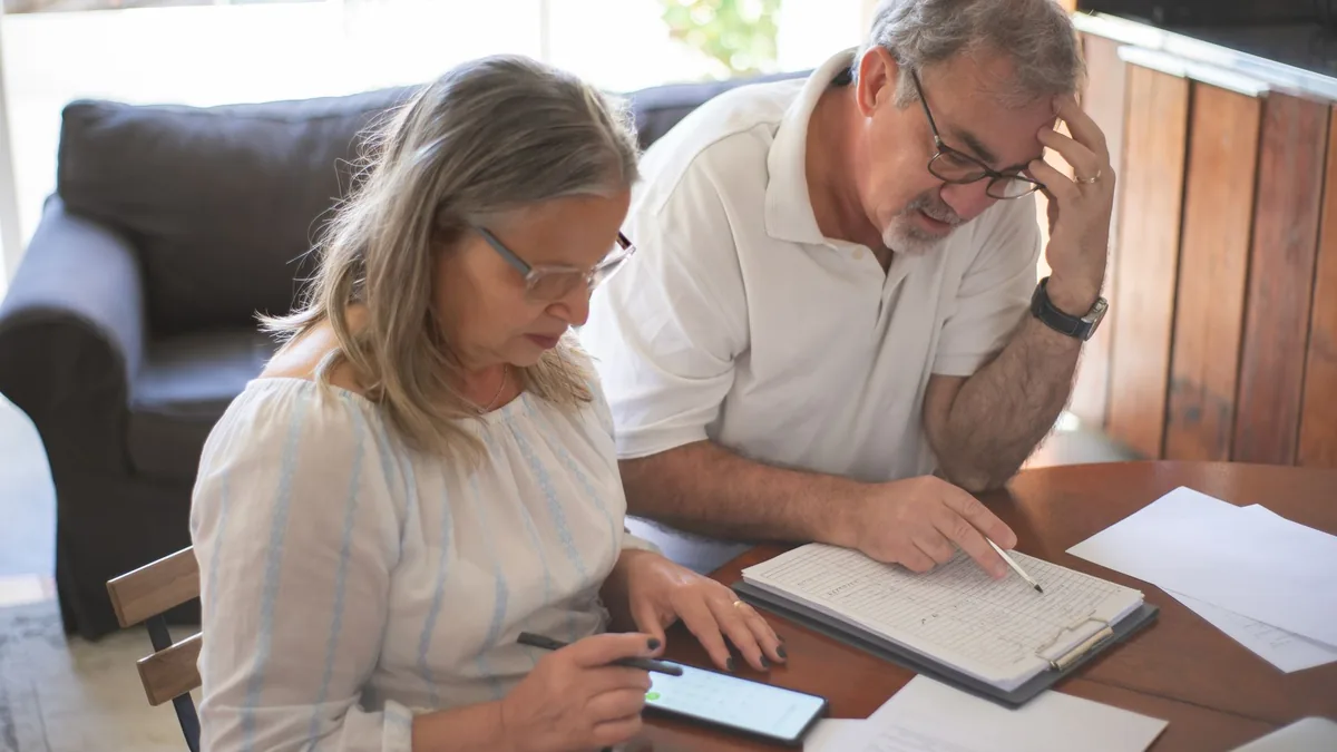 Older couple going through bills and paperwork together at home with a tablet