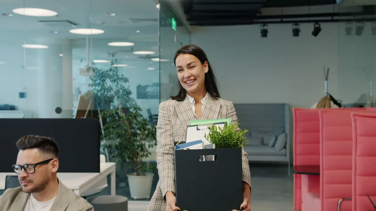 Happy woman carrying a box and plant into a new office on her first day
