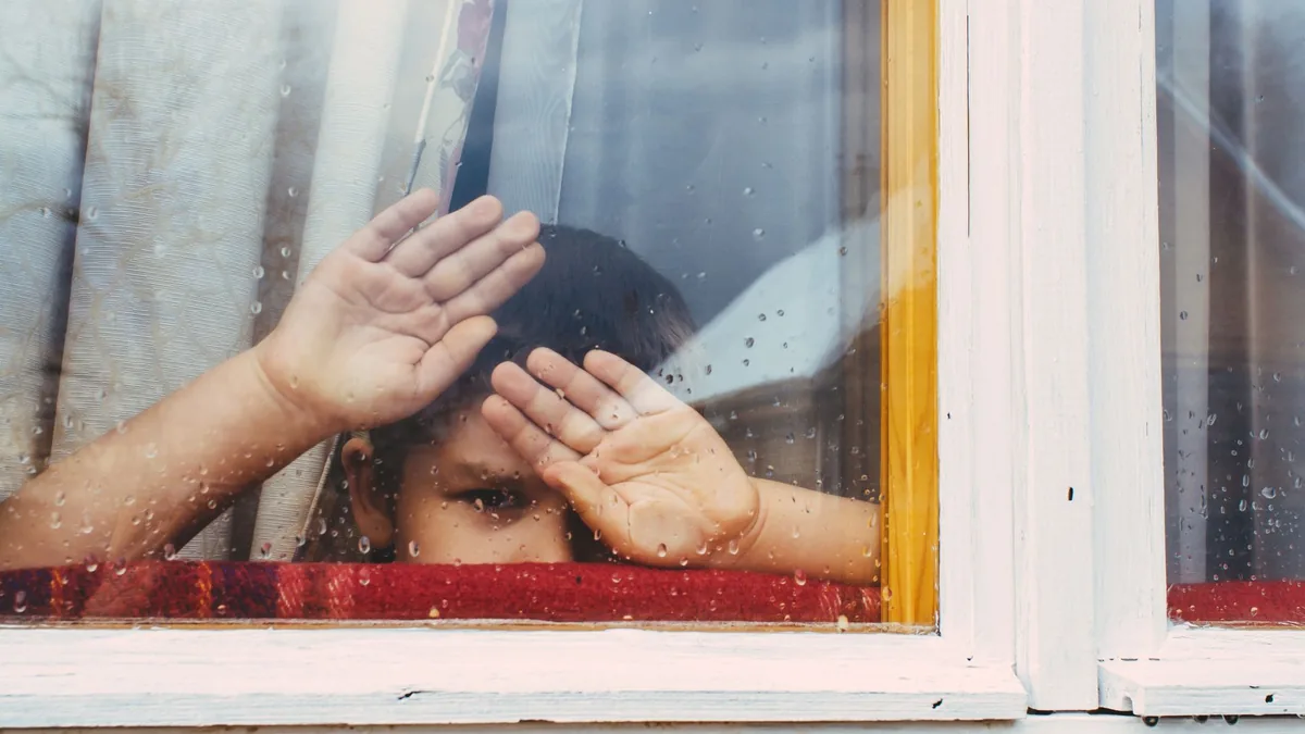 Young boy looking out of a rain-speckled window