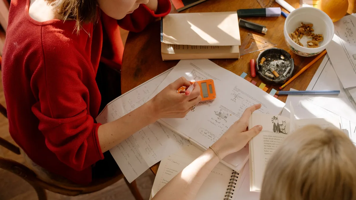 Two students revising at a table covered with textbooks and notes