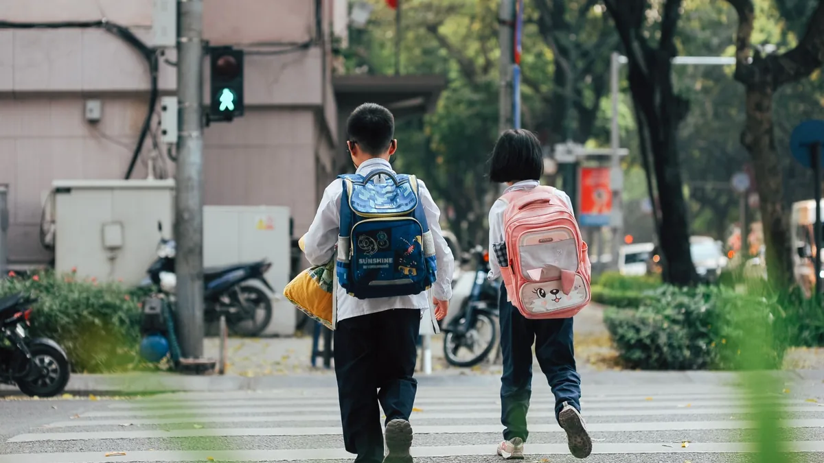 Two children with school backpacks crossing the road at a pedestrian crossing