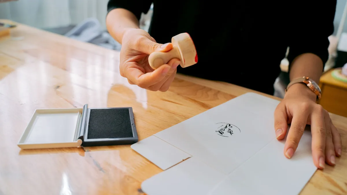Hands using a rubber stamp on paper at a wooden table