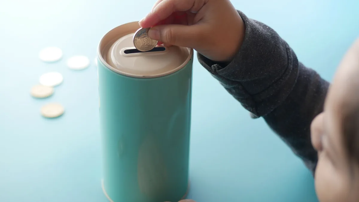Child dropping a coin into a teal money box