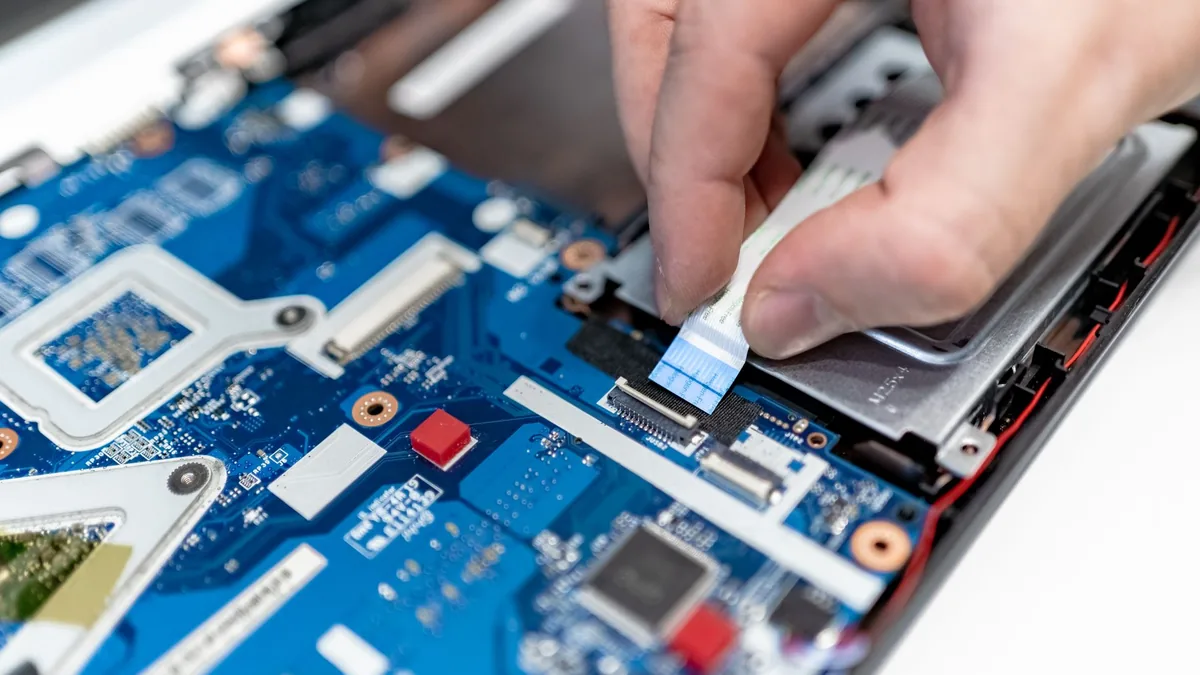 Hands repairing the circuit board of an open laptop