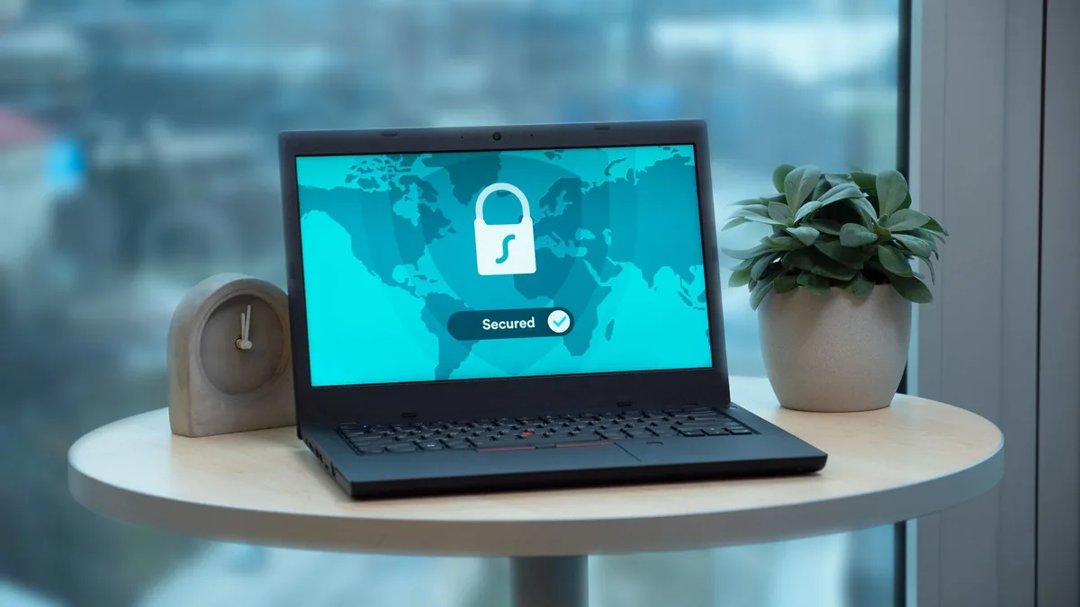 Laptop showing a padlock security icon on a table beside a plant and clock