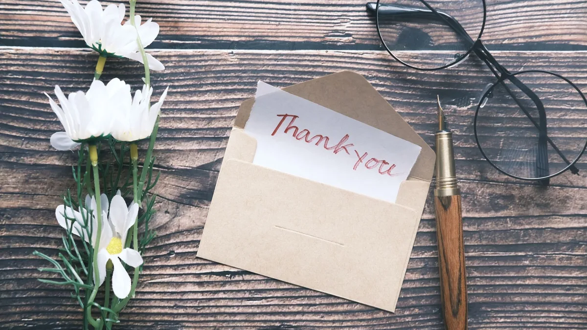 Thank-you note in a kraft envelope with daisies, glasses and a pen on a wooden table