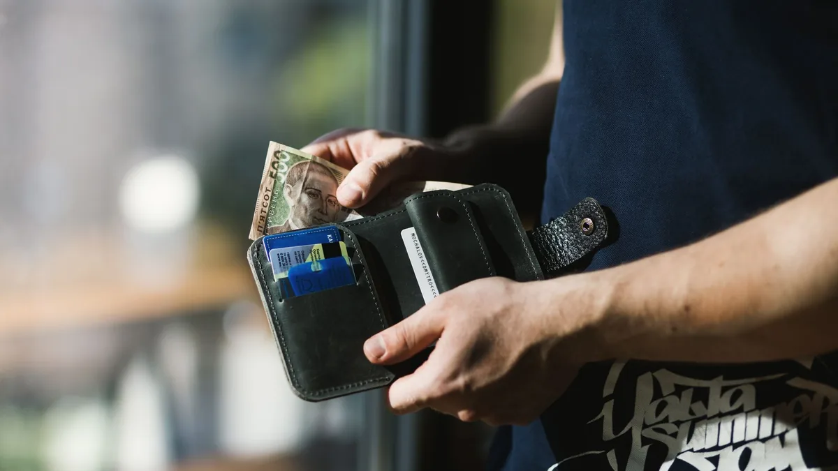 Man taking cash out of a wallet that also holds bank cards