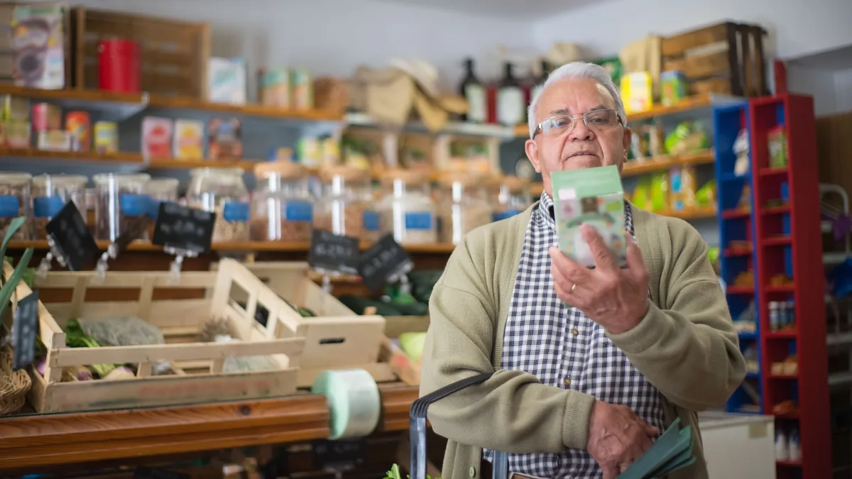 Older man reading the label on a product in a supermarket aisle