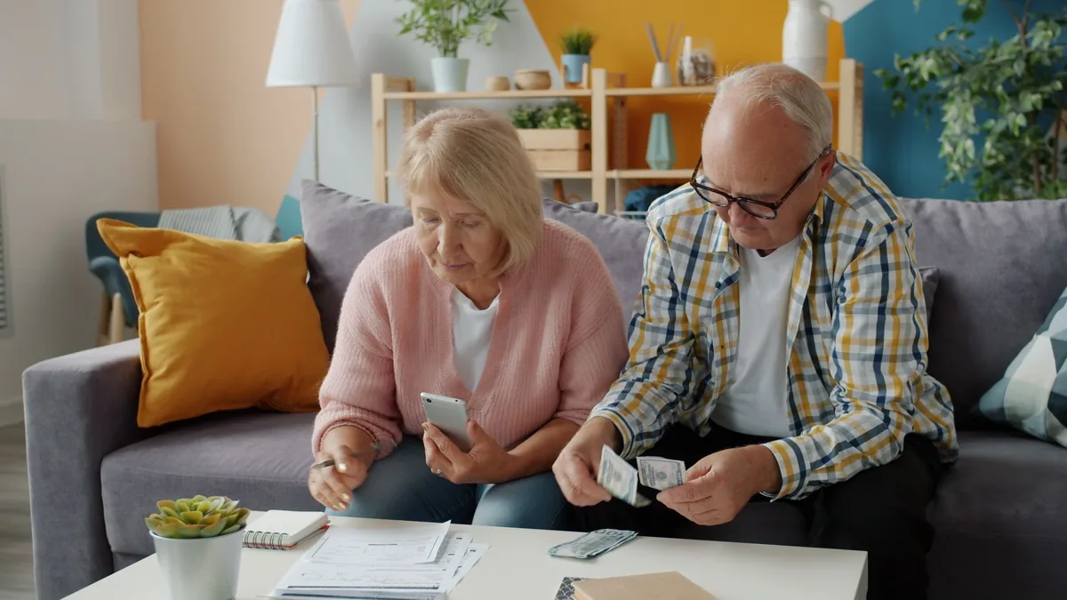 Older couple sitting on a sofa going through their finances with a phone and cash