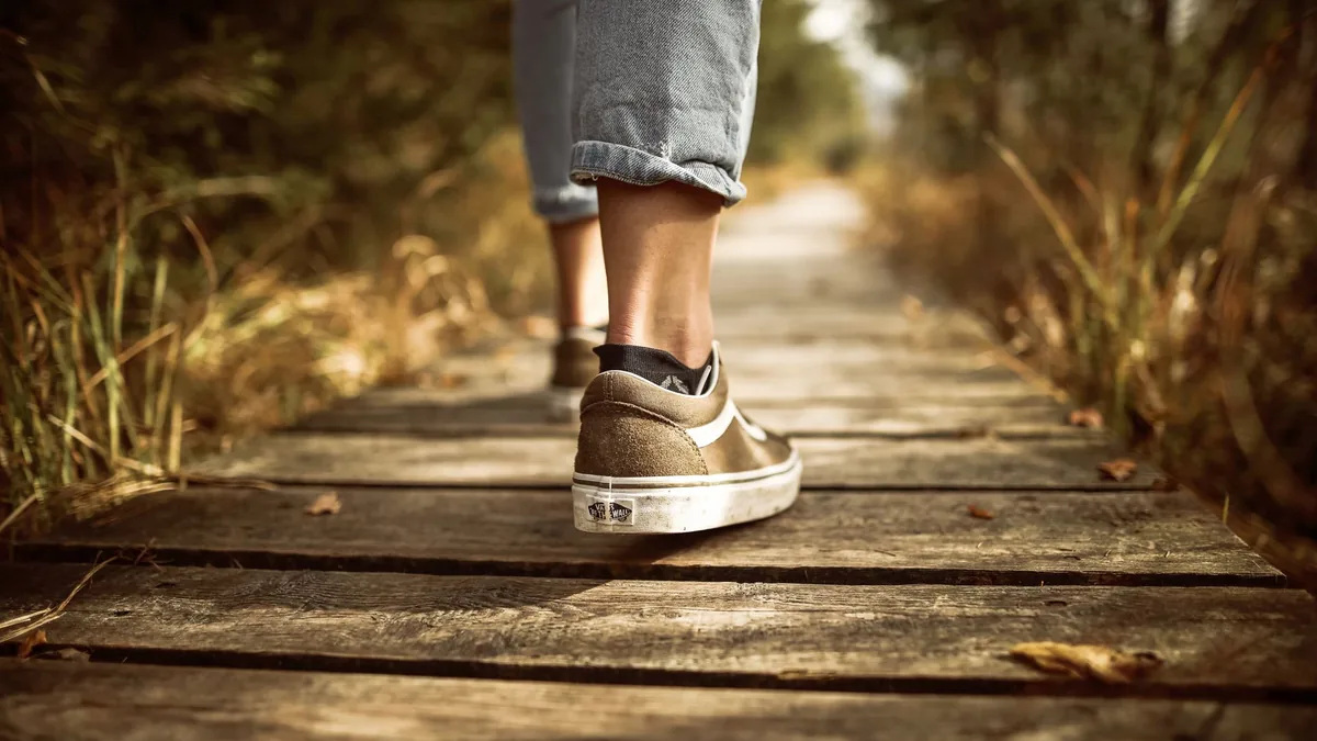Close-up of trainers walking along a sunlit wooden path in a park