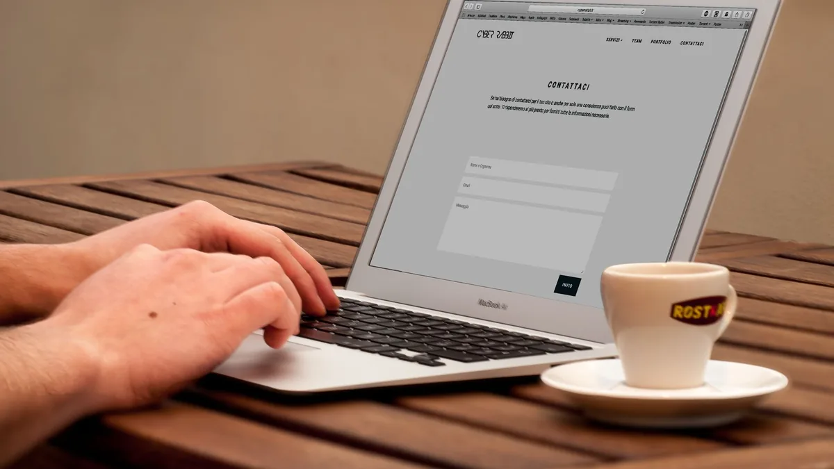 Hands typing on a laptop next to a cup of coffee on a wooden desk