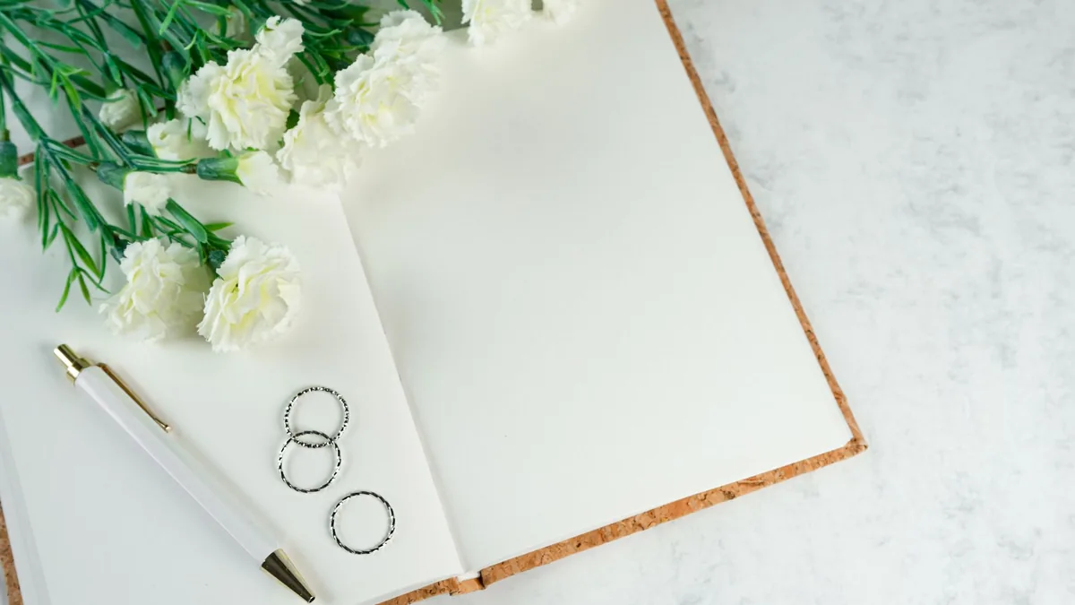 Open notebook with wedding rings and white flowers on a marble table